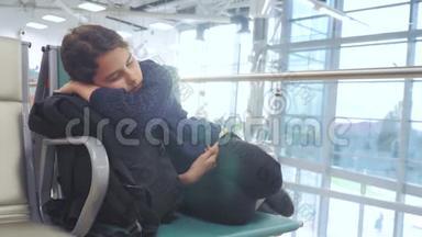 疲惫的少女少年旅行者睡在机场，等待飞机起飞，登机口的长椅上，她的行李都在她身边